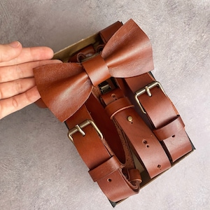 May include: A brown leather bow tie and suspenders set. The bow tie is tied and the suspenders are adjustable with brass buckles.