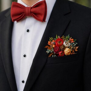 May include: A black suit jacket worn over a white dress shirt with black buttons. The outfit features a solid dark red bow tie and a pocket square arrangement consisting of artificial red, orange, and yellow flowers with green foliage.