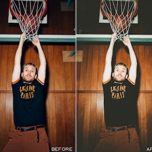 K&ouml;nnte beinhalten: Eine Person tr&auml;gt ein schwarzes T-Shirt mit dem Text "Leine Paris" in gelben Buchstaben, eine braune Hose und einen schwarzen G&uuml;rtel und springt hoch, um einen Basketball zu dunken. Die Person befindet sich in einer Sporthalle mit Holzvert&auml;felung an den W&auml;nden.