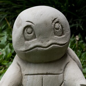 Pu&ograve; includere: Una scultura di tartaruga in pietra grigia con un'espressione amichevole. La scultura &egrave; dettagliata con un guscio e occhi.