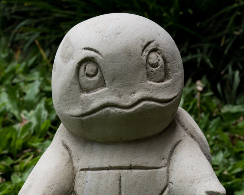 Pu&ograve; includere: Una scultura di tartaruga in pietra grigia con un'espressione amichevole. La scultura &egrave; dettagliata con un guscio e occhi.