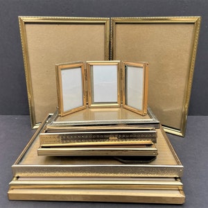 May include: A set of gold-toned picture frames, with a larger frame in the back and a smaller, multi-panel frame in the front. The frames are stacked on top of each other, creating a tiered display.