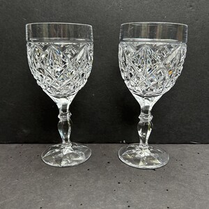 May include: Two clear glass wine glasses with a cut crystal design. The glasses have a round bowl and a tall stem.