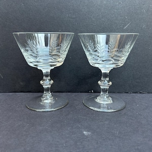 May include: Two clear glass stemmed cocktail glasses with an etched wheat design.