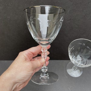 May include: Two clear glass wine glasses with etched designs. The glass on the left has a silver rim and a stemmed base. The glass on the right has a shorter stem and a wider bowl.