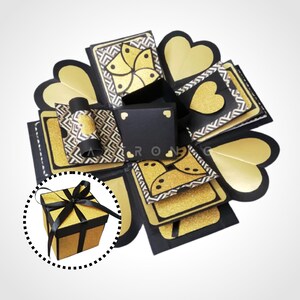 May include: A black and gold explosion box with a heart-shaped design. The box is decorated with glitter and has a small gift box inside.