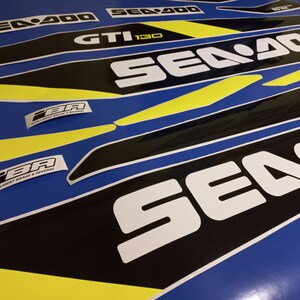 May include: A set of black and yellow Sea-Doo decals with the text "Sea-Doo" and "GTI 130" in white. The decals are on a blue background.