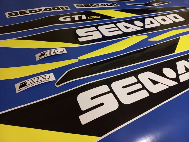 May include: A set of black and yellow Sea-Doo decals with the text "Sea-Doo" and "GTI 130" in white. The decals are on a blue background.