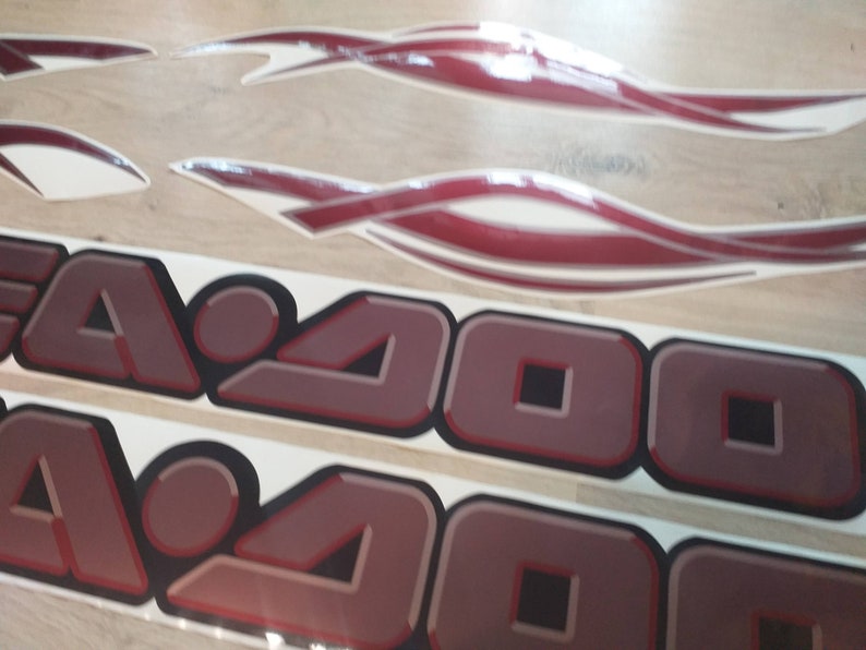 May include: Two red and white decals with the text "Sea-Doo" in a 3D-style font. The decals are on a white background.