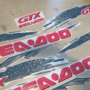 K&ouml;nnte beinhalten: Ein Satz roter und grauer Vinyl-Aufkleber f&uuml;r ein Sea-Doo GTX Sea-Doo 900 Wasserfahrzeug. Die Aufkleber zeigen das Sea-Doo-Logo und den Text "GTX Sea-Doo 900".
