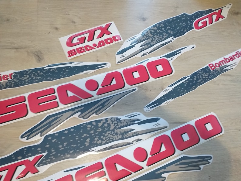 K&ouml;nnte beinhalten: Ein Satz roter und grauer Vinyl-Aufkleber f&uuml;r ein Sea-Doo GTX Sea-Doo 900 Wasserfahrzeug. Die Aufkleber zeigen das Sea-Doo-Logo und den Text "GTX Sea-Doo 900".