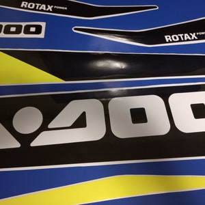 May include: A black and white graphic with the text "A 900" in white letters on a black background. The graphic is on a blue and yellow background with the text "ROTAX POWER" in black letters on a white background.
