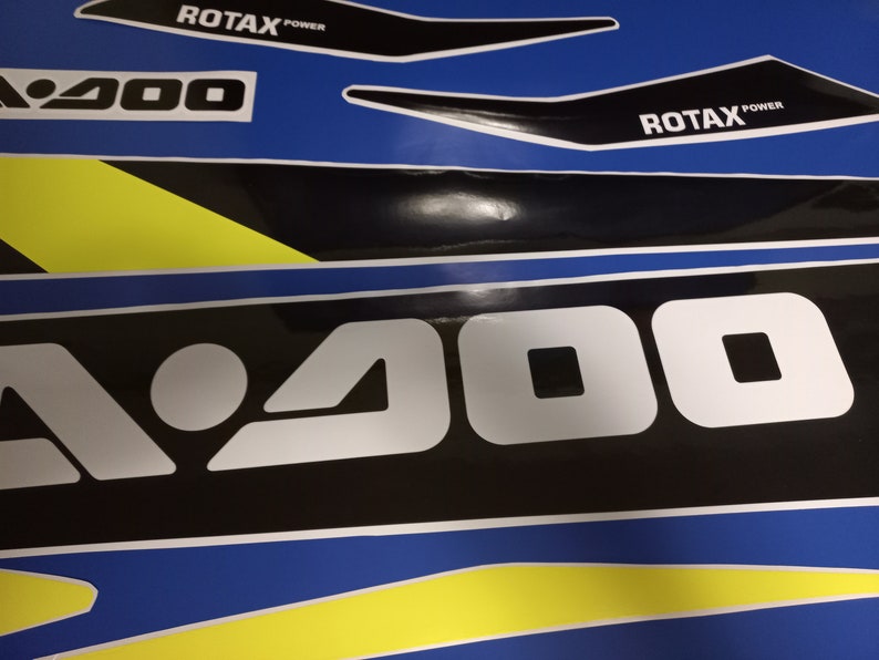 May include: A black and white graphic with the text "A 900" in white letters on a black background. The graphic is on a blue and yellow background with the text "ROTAX POWER" in black letters on a white background.
