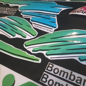 Puede incluir: Un conjunto de calcoman&iacute;as verdes, azules y blancas con el texto "Sea-Doo" y "Powered by Rotax". Las calcoman&iacute;as est&aacute;n dise&ntilde;adas para una moto de nieve o una embarcaci&oacute;n.