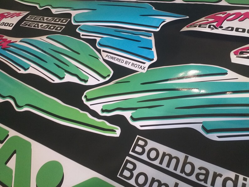 Puede incluir: Un conjunto de calcoman&iacute;as verdes, azules y blancas con el texto "Sea-Doo" y "Powered by Rotax". Las calcoman&iacute;as est&aacute;n dise&ntilde;adas para una moto de nieve o una embarcaci&oacute;n.