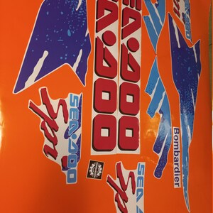 K&ouml;nnte beinhalten: Ein Satz Sea-Doo Sport-Aufkleber in Blau, Rot und Wei&szlig;. Die Aufkleber zeigen das Sea-Doo-Logo und die Worte "Sea-Doo Sport" und "Bombardier".