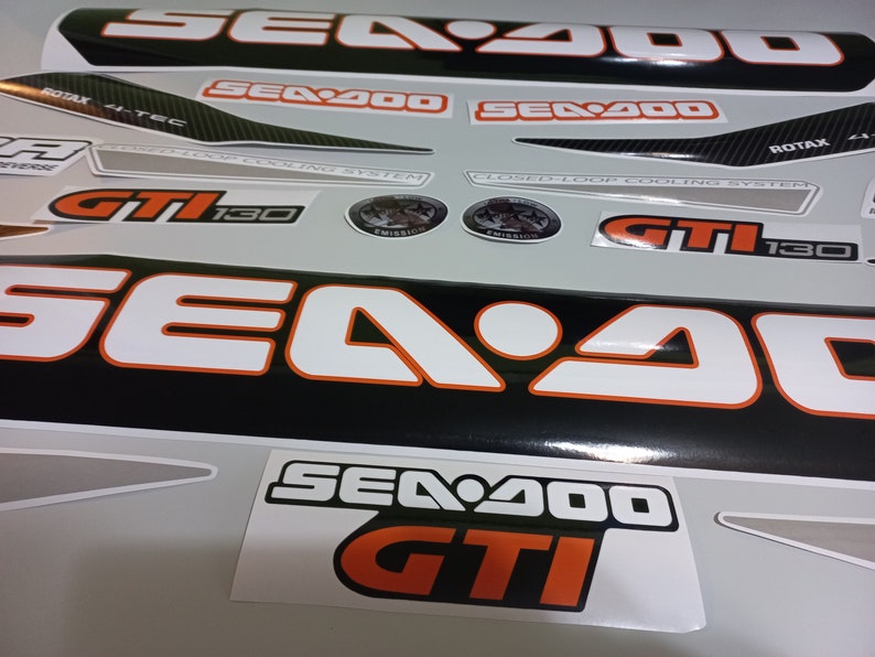 May include: A set of black and white Sea-Doo GTI 130 decals with orange accents. The decals feature the Sea-Doo logo, the model name, and the engine size. The decals are designed to be applied to a Sea-Doo watercraft.
