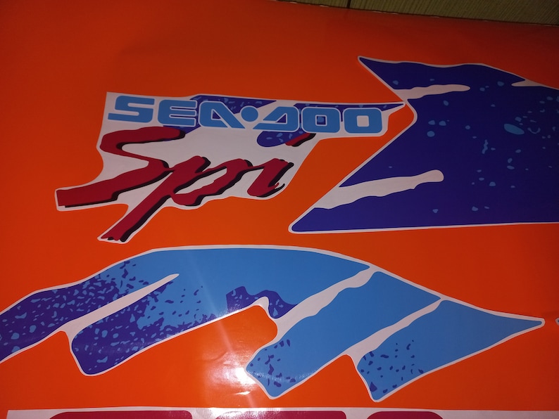 K&ouml;nnte beinhalten: Eine blaue und wei&szlig;e Grafik mit dem Text "SEA-DOO Sport" in Rot und Blau auf orangefarbenem Hintergrund.