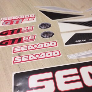 May include: A set of white and black decals with red accents. The decals feature the text "Sea-Doo", "GTISE", and "ROTAX 4-TEC".