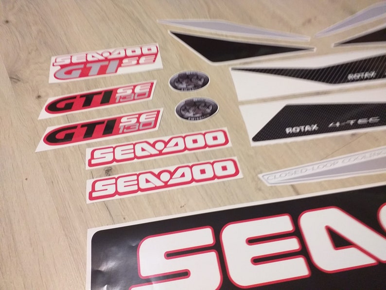 May include: A set of white and black decals with red accents. The decals feature the text "Sea-Doo", "GTISE", and "ROTAX 4-TEC".