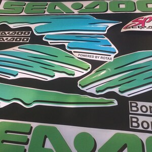 Puede incluir: Un conjunto de calcoman&iacute;as Sea-Doo verdes, azules y blancas con el texto "Sea-Doo", "Sea-Doo SPX", "Powered by Rotax" y "Bombardier" sobre un fondo negro.
