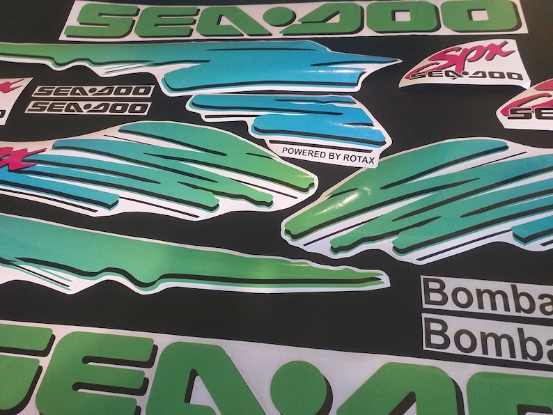 Puede incluir: Un conjunto de calcoman&iacute;as Sea-Doo verdes, azules y blancas con el texto "Sea-Doo", "Sea-Doo SPX", "Powered by Rotax" y "Bombardier" sobre un fondo negro.