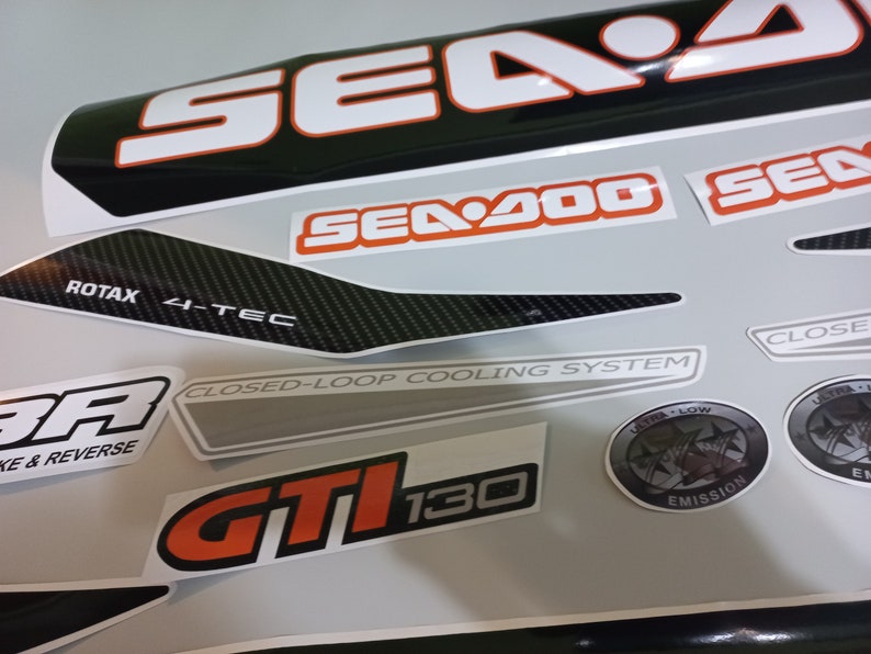 May include: A set of black and white Sea-Doo decals with orange accents. The decals include the words "Sea-Doo", "Sea-Doo 4-Tec", "GT1130", "Closed-Loop Cooling System", "Ultra Low Emission", and "Rotax 4-Tec".
