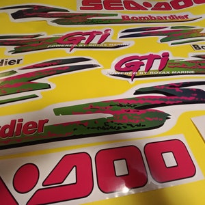 May include: A set of Sea-Doo GTI decals in pink, green, and black. The decals feature the Sea-Doo logo, the words "GTI" and "Powered by Rotax Marine", and the word "Bombardier".