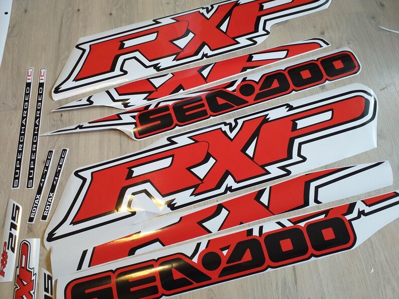 May include: A set of red and black vinyl decals for a Sea-Doo watercraft. The decals feature the words "Sea-Doo" and "RXP" in a bold, stylized font. The decals are designed to be applied to the hull of a Sea-Doo watercraft.