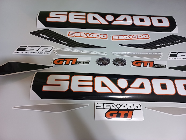 May include: A set of black and white Sea-Doo decals with orange accents. The decals feature the Sea-Doo logo, the text "Sea-Doo", "Sea-Doo GTI", "GT1 130", "Closed-Loop Cooling System", "Rotax 4-Tec", and "Intelligent Brake & Reverse".