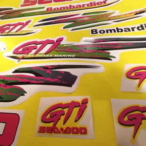 May include: A set of pink, green, and black decals for a Sea-Doo GTI jet ski. The decals feature the Sea-Doo logo, the GTI logo, and the text "Powered by Rotax Marine".