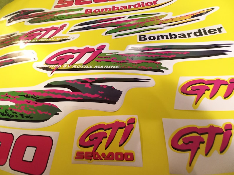 May include: A set of pink, green, and black decals for a Sea-Doo GTI jet ski. The decals feature the Sea-Doo logo, the GTI logo, and the text "Powered by Rotax Marine".