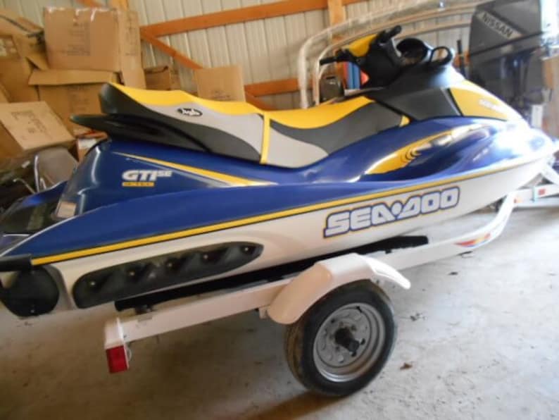 May include: A blue and white Sea-Doo GTI SE watercraft with yellow accents. The jet ski is on a trailer with a single wheel.