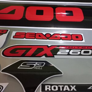 May include: A close-up of various Sea-Doo decals, including a black and red "Sea-Doo GTX 260 Limited" sticker, a black and white "S3 Hull" sticker, and a black and white "ROTAX 4-TEC" sticker.