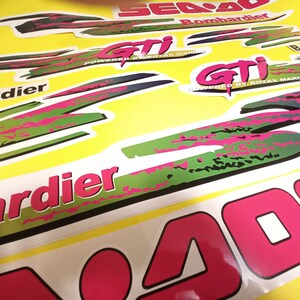 May include: A close-up of a Sea-Doo 400 jet ski decal set. The decals are green, pink, and black with the text "Sea-Doo 400" and "Bombardier" in white. The decals are designed to be applied to a jet ski.