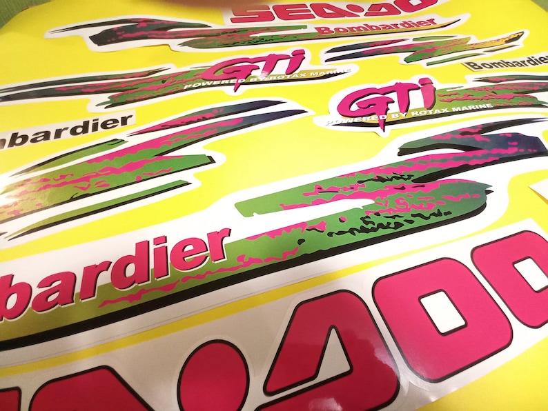 May include: A close-up of a Sea-Doo 400 jet ski decal set. The decals are green, pink, and black with the text "Sea-Doo 400" and "Bombardier" in white. The decals are designed to be applied to a jet ski.