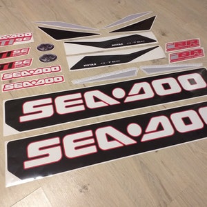 May include: A set of black and white Sea-Doo decals with red accents. The decals include the Sea-Doo logo, the words "Sea-Doo", "GTISE", and "ROTAX 4-TEC".
