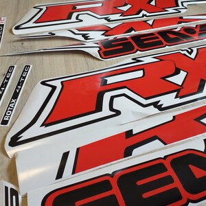May include: A set of red and black vinyl decals with the words "Supercharged", "Supercharged IC", "Rotax 4-Tec", "Rotax 4-Tec", and "RX1" in white lettering. The decals are designed for a vehicle or other surface.