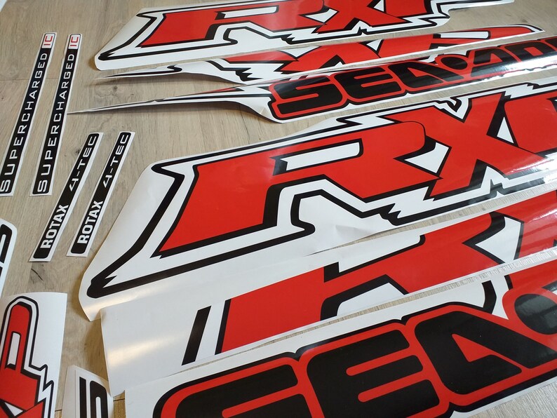 May include: A set of red and black vinyl decals with the words "Supercharged", "Supercharged IC", "Rotax 4-Tec", "Rotax 4-Tec", and "RX1" in white lettering. The decals are designed for a vehicle or other surface.