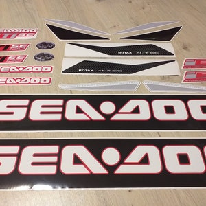 May include: A set of black and white decals with red accents for a Sea-Doo watercraft. The decals include the words "Sea-Doo", "GTISE", "ROTAX", and "Intelligent Brake & Reverse".