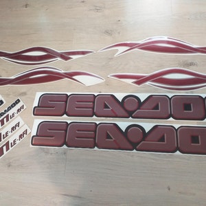 May include: A set of red and white Sea-Doo decals. The decals include the words "Sea-Doo" and "GT LE-RFI".