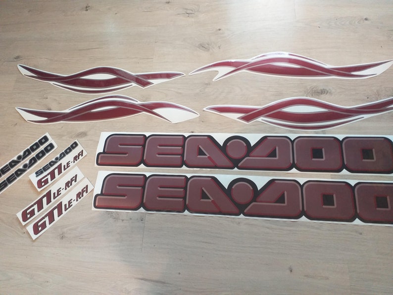 May include: A set of red and white Sea-Doo decals. The decals include the words "Sea-Doo" and "GT LE-RFI".