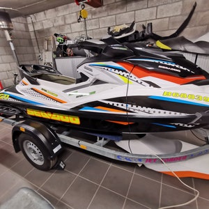 May include: A white, black, orange and blue Sea-Doo Spark jet ski with a black and white graphic design. The jet ski is on a trailer with a black tyre and the registration number B68839.