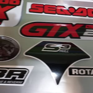 May include: A collection of stickers featuring various logos and designs. The stickers are black, white, red, and gray. The logos include "Sea-Doo", "GTX", "Limit 260", "S3 Hull", "BR", and "Rotax".