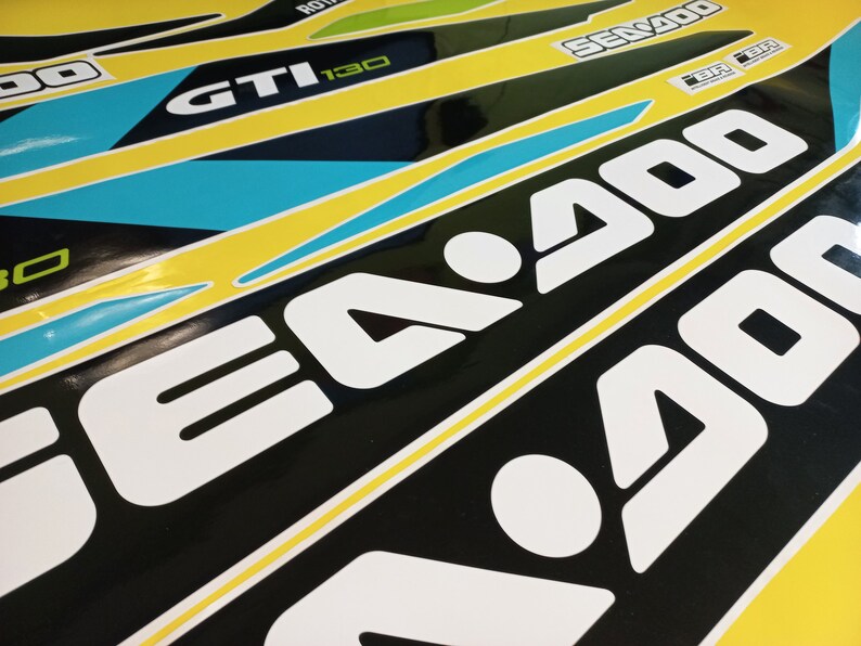 以下が含まれることがあります： 黄色い背景に白い文字で「SEA-DOO」と書かれた黒と白のステッカーのクローズアップ。このステッカーは、黄色い背景に黒い文字で「GTI 130」と「SEA-DOO」と書かれたステッカーの大きなセットの一部です。
