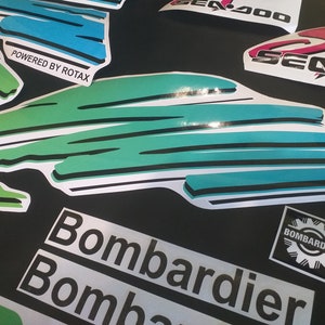 Puede incluir: Un conjunto de calcoman&iacute;as para una moto acu&aacute;tica Sea-Doo. Las calcoman&iacute;as son blancas con acentos verdes, azules y rosas. Las calcoman&iacute;as presentan las palabras "Sea-Doo", "Bombardier" y "Powered by Rotax".