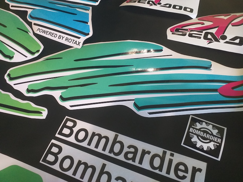 Puede incluir: Un conjunto de calcoman&iacute;as para una moto acu&aacute;tica Sea-Doo. Las calcoman&iacute;as son blancas con acentos verdes, azules y rosas. Las calcoman&iacute;as presentan las palabras "Sea-Doo", "Bombardier" y "Powered by Rotax".