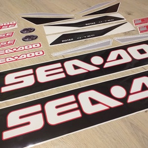 May include: A set of black and white Sea-Doo decals with red accents. The decals feature the Sea-Doo logo and the text "Sea-Doo" and "Sea-Doo 900".