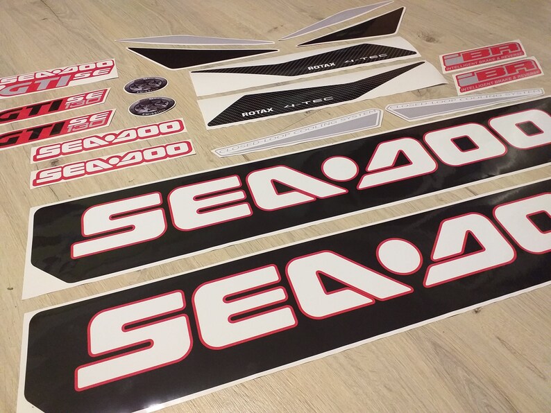 May include: A set of black and white Sea-Doo decals with red accents. The decals feature the Sea-Doo logo and the text "Sea-Doo" and "Sea-Doo 900".