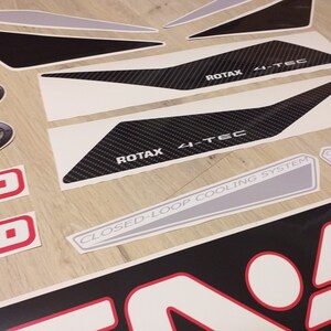 May include: A set of black and white decals with a carbon fiber pattern and the text "ROTAX 4-TEC" and "CLOSED-LOOP COOLING SYSTEM".